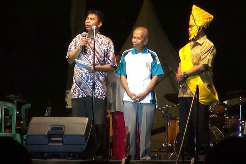 Asman Yodjodolo (tengah), penyintas Peristiwa 1965/1966 dari Kota Palu, saat diberi kesempatan oleh Wali Kota Palu, Rusdy Mastura (berpakaian kuning), untuk tampil di atas panggung dan menyampaikan pidato pada Peringatan Hari Ulang Tahun Kota Palu.